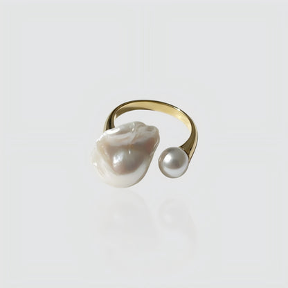 Woman's hand wearing a gold open ring with one large baroque pearl and one small round pearl.