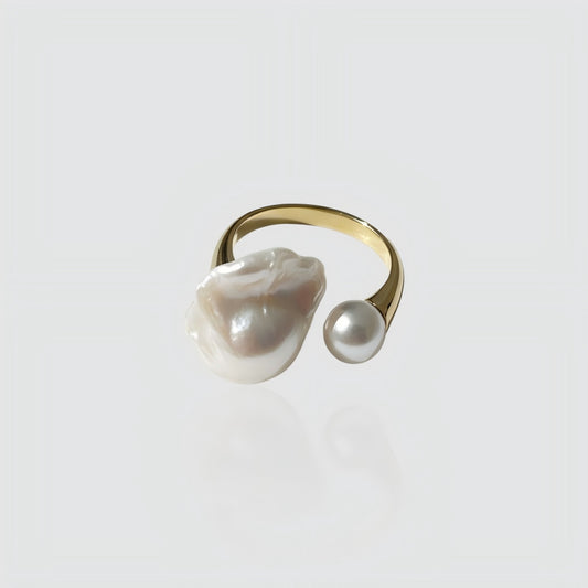 Woman's hand wearing a gold open ring with one large baroque pearl and one small round pearl.