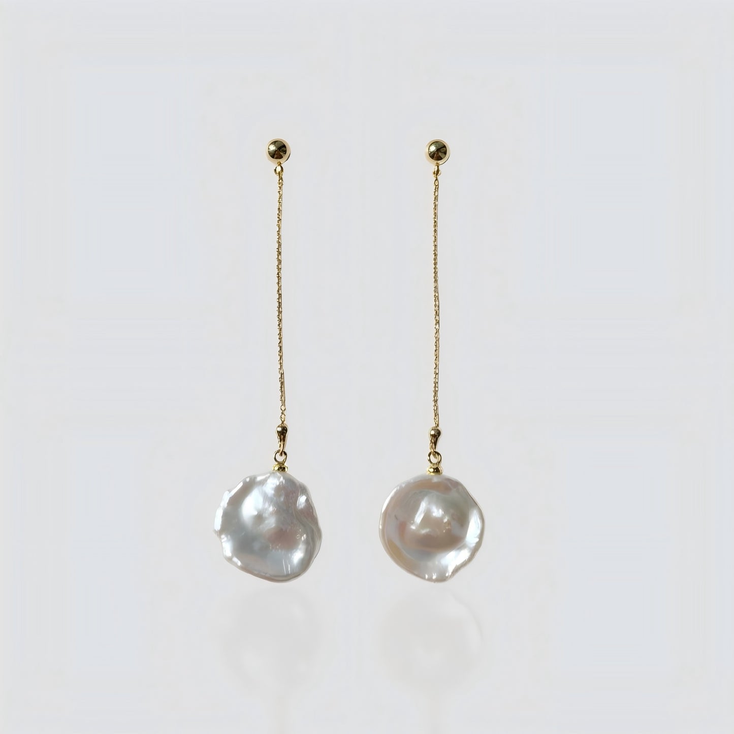 A pair of elegant gold chain drop earrings with irregular freshwater baroque pearls, presented on a soft grey background for clear product viewing.