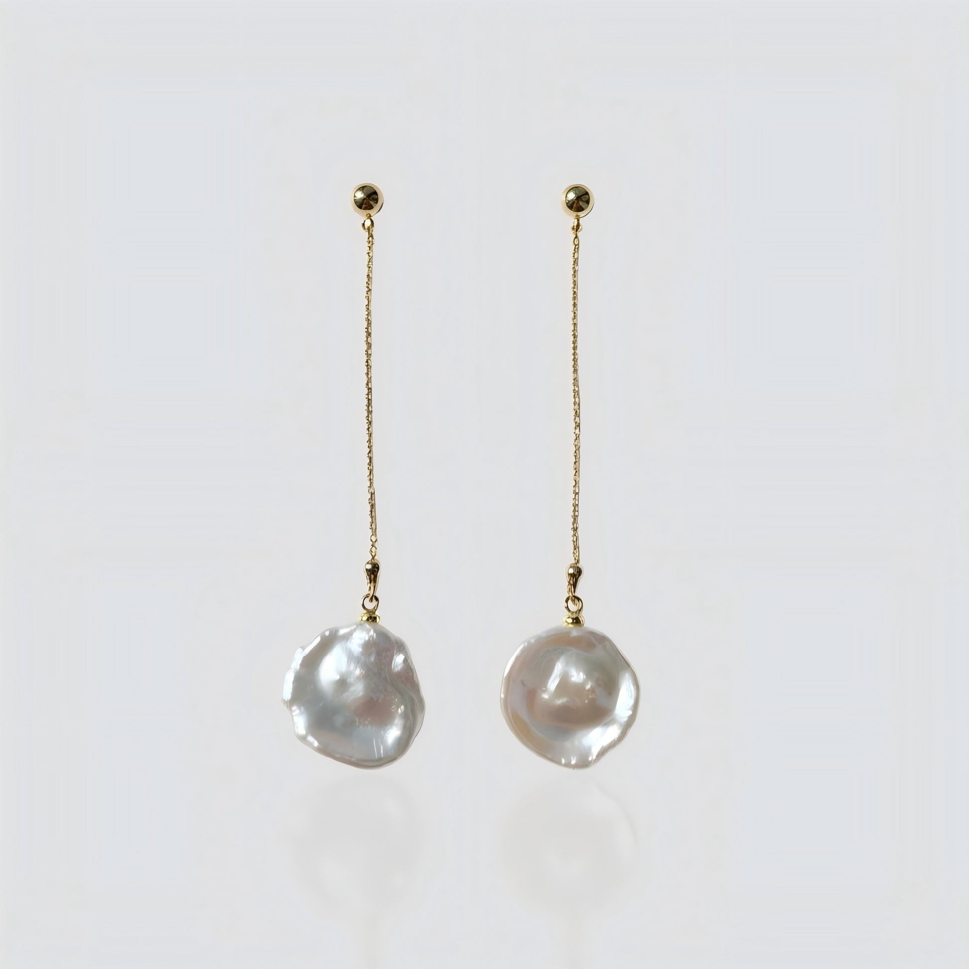 A pair of elegant gold chain drop earrings with irregular freshwater baroque pearls, presented on a soft grey background for clear product viewing.
