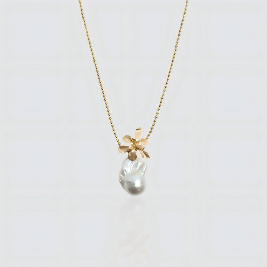 A white freshwater baroque pearl pendant topped with a sculpted gold flower design, hanging on a gold beaded satellite chain against a white background.