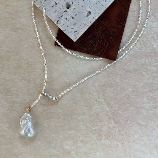 Macro photography showing the texture of tiny rice pearls, the sparkle of the gold pave bar connector, and the iridescent luster of the large baroque pearl drop.