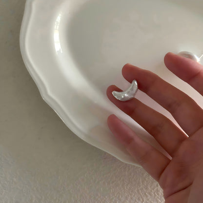 Hand holding a small, organic crescent moon pearl earring, showing the natural texture and luster.