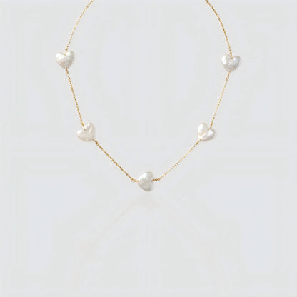 Studio shot of a gold chain necklace featuring multiple flat white heart-shaped pearls spaced out on a grey background.