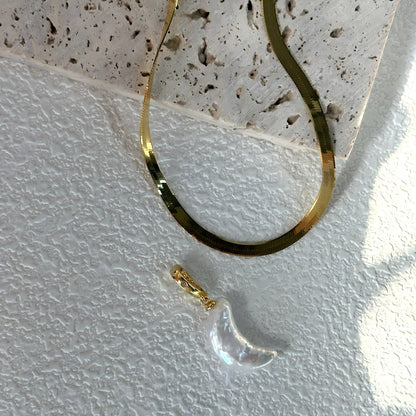 Close-up macro shot showing the texture of the flat gold herringbone chain and the nacre of the crescent moon pearl.