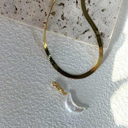 Close-up macro shot showing the texture of the flat gold herringbone chain and the nacre of the crescent moon pearl.