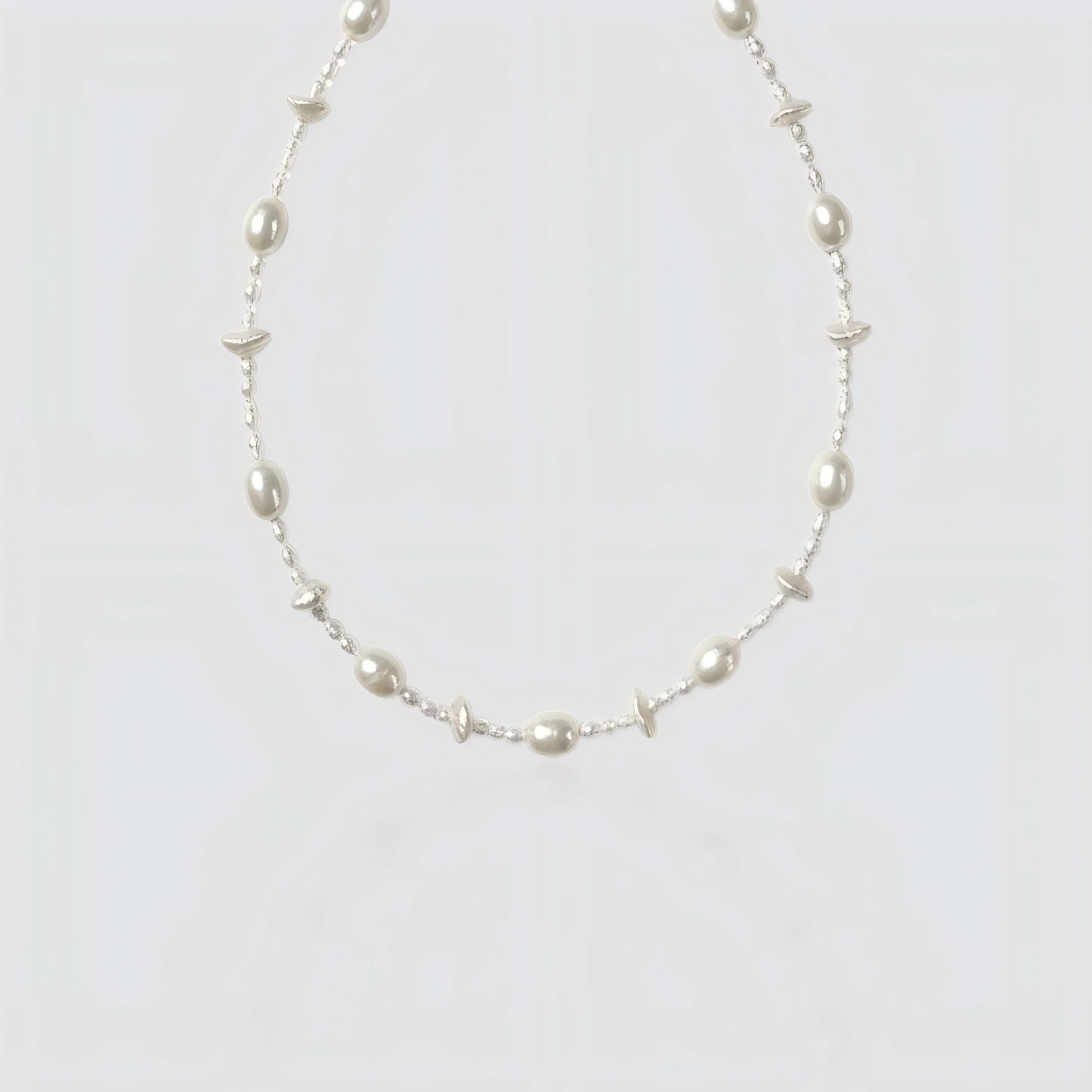 Studio shot of a beaded necklace featuring alternating large white freshwater pearls and tiny clear seed beads on a grey background.