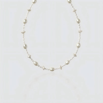 Studio shot of a beaded necklace featuring alternating large white freshwater pearls and tiny clear seed beads on a grey background.