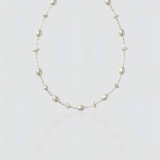 Studio shot of a beaded necklace featuring alternating large white freshwater pearls and tiny clear seed beads on a grey background.