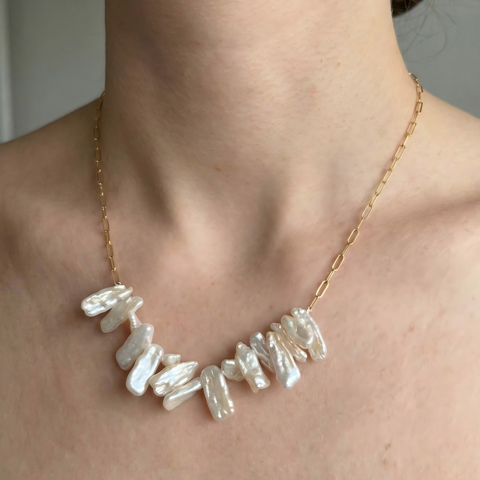 A stylish woman wearing the gold paperclip chain necklace with the cluster of stick pearls as a statement piece over a black top.