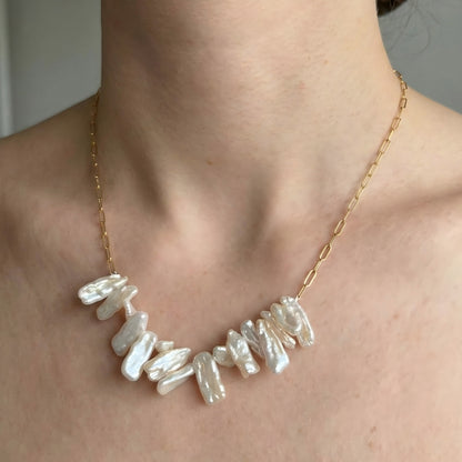 A stylish woman wearing the gold paperclip chain necklace with the cluster of stick pearls as a statement piece over a black top.