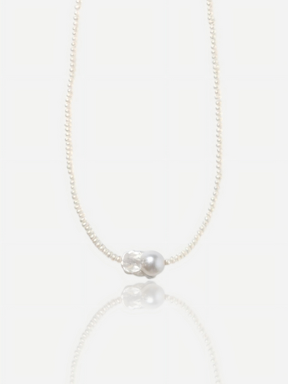 Close-up of Pearltide Azure Aura necklace featuring a large textured "crushed silver" baroque pearl centerpiece surrounded by delicate tiny seed pearls on a white background with a soft reflection, elegant quiet luxury jewelry.