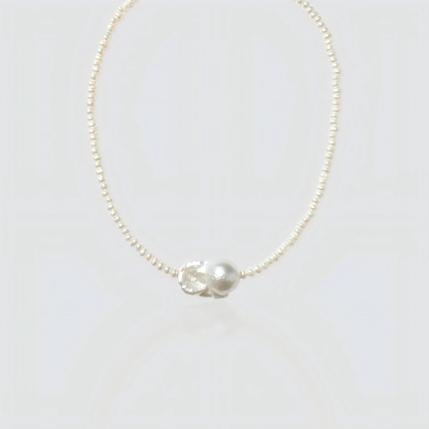Studio shot of a natural baroque pearl necklace on a neutral grey background, showing the irregular organic pearl pendant.