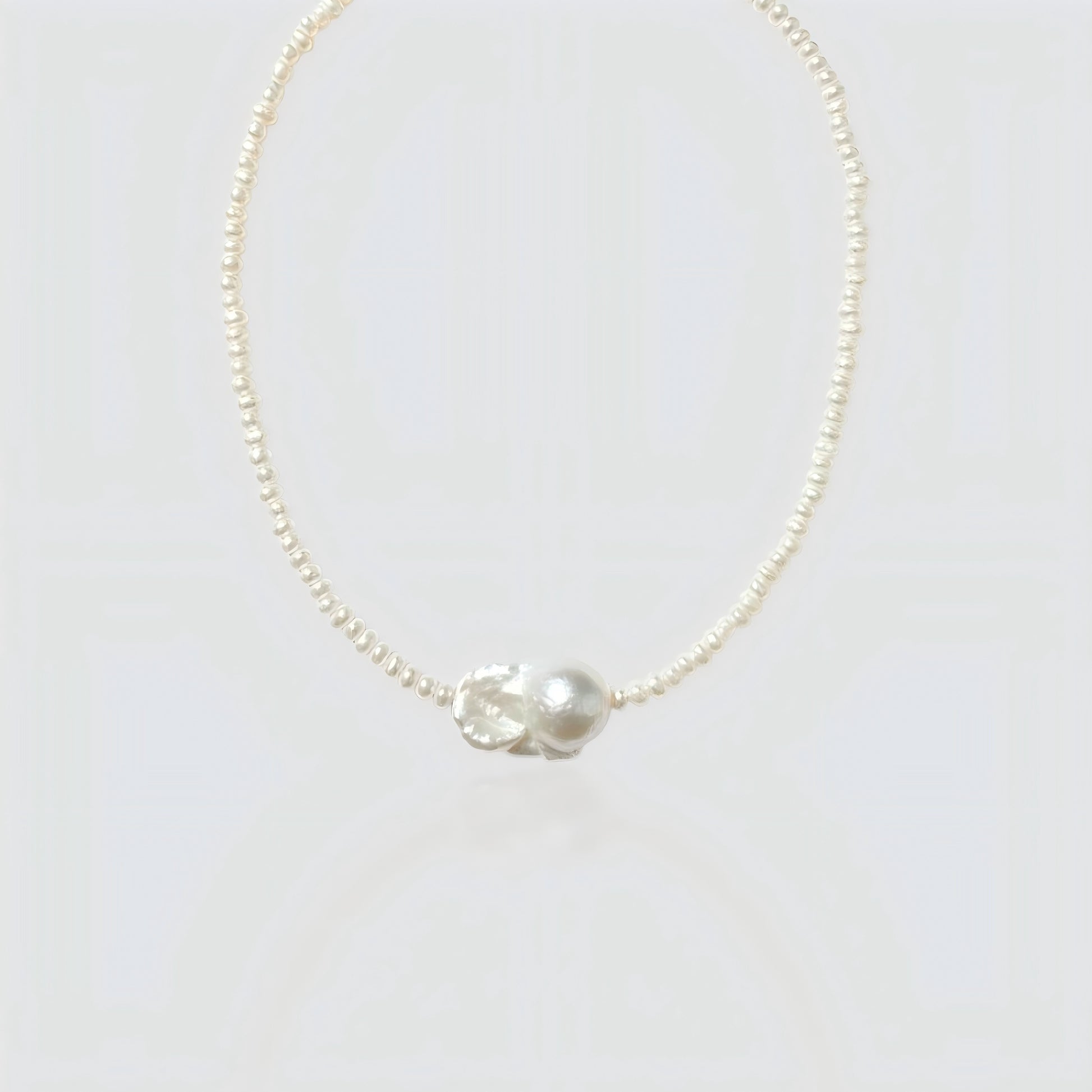 Studio shot of a natural baroque pearl necklace on a neutral grey background, showing the irregular organic pearl pendant.