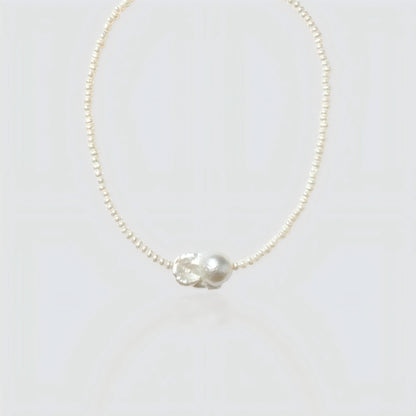 Studio shot of a natural baroque pearl necklace on a neutral grey background, showing the irregular organic pearl pendant.