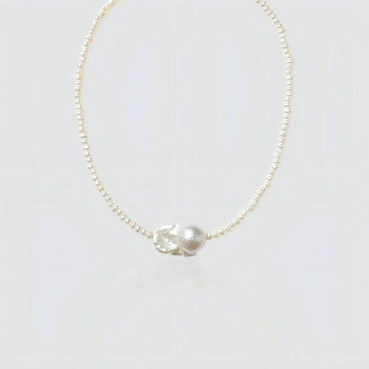 Studio shot of a natural baroque pearl necklace on a neutral grey background, showing the irregular organic pearl pendant.