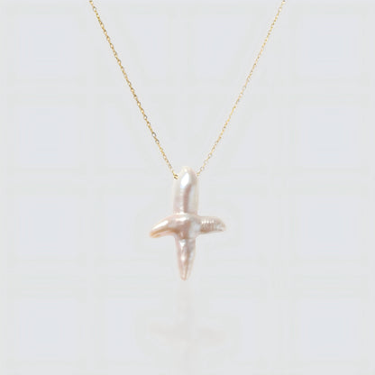 A white background product shot of a unique cross-shaped baroque pearl pendant on a delicate gold chain.