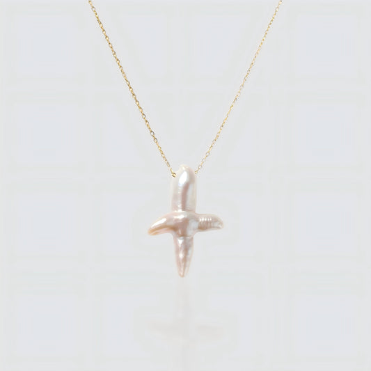 A white background product shot of a unique cross-shaped baroque pearl pendant on a delicate gold chain.
