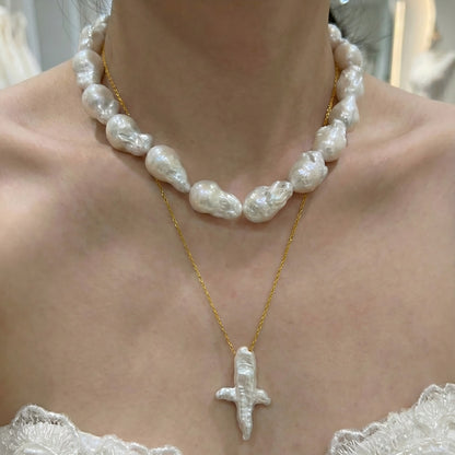 A woman wearing a dainty gold necklace with an abstract star-shaped pearl pendant, styled with a casual chic outfit.