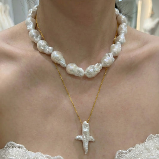 A woman wearing a dainty gold necklace with an abstract star-shaped pearl pendant, styled with a casual chic outfit.