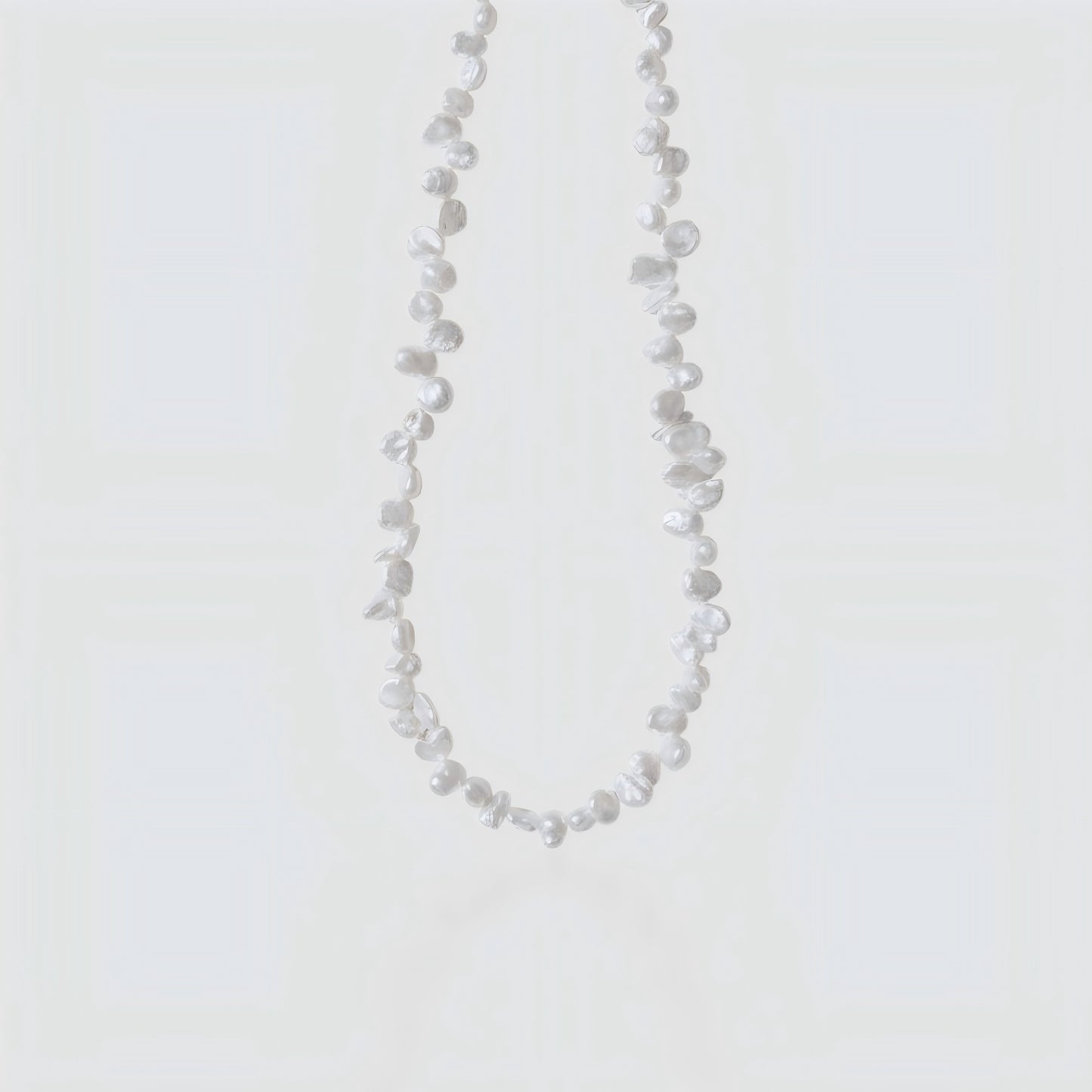 Studio shot of a white Keshi pearl necklace with irregular petal shapes and high luster on a neutral grey background.