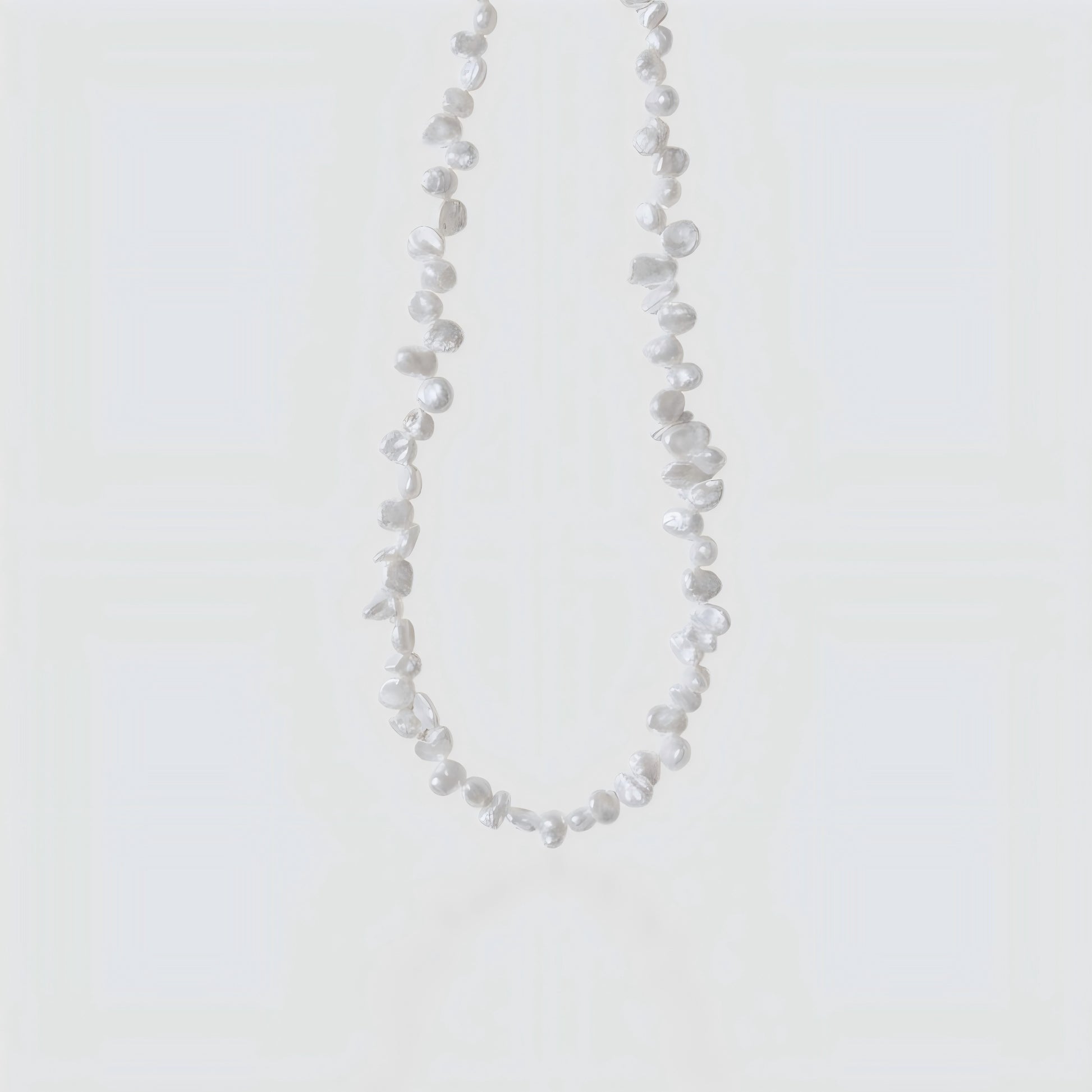 Studio shot of a white Keshi pearl necklace with irregular petal shapes and high luster on a neutral grey background.