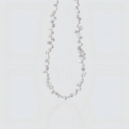 Studio shot of a white Keshi pearl necklace with irregular petal shapes and high luster on a neutral grey background.