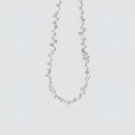 Studio shot of a white Keshi pearl necklace with irregular petal shapes and high luster on a neutral grey background.