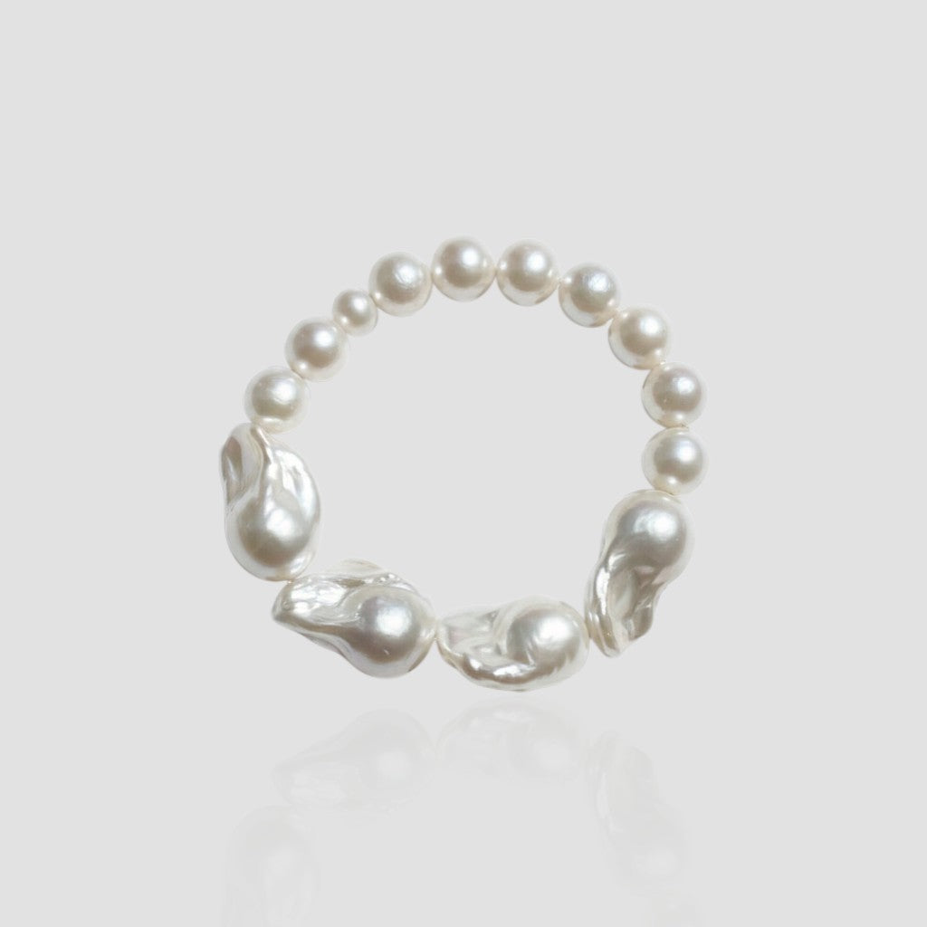 Studio shot of a white freshwater pearl bracelet on a light grey background, featuring a unique half-round, half-baroque pearl design.