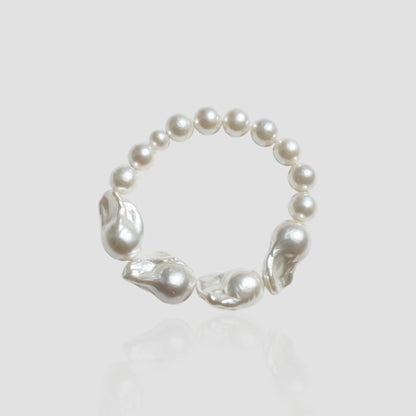 Studio shot of a white freshwater pearl bracelet on a light grey background, featuring a unique half-round, half-baroque pearl design.