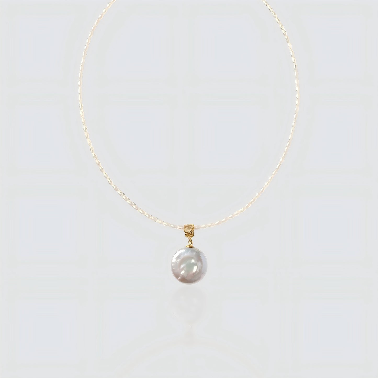 A pristine view of our delicate seed pearl strand featuring a large, lustrous coin pearl pendant with a textured gold bail.