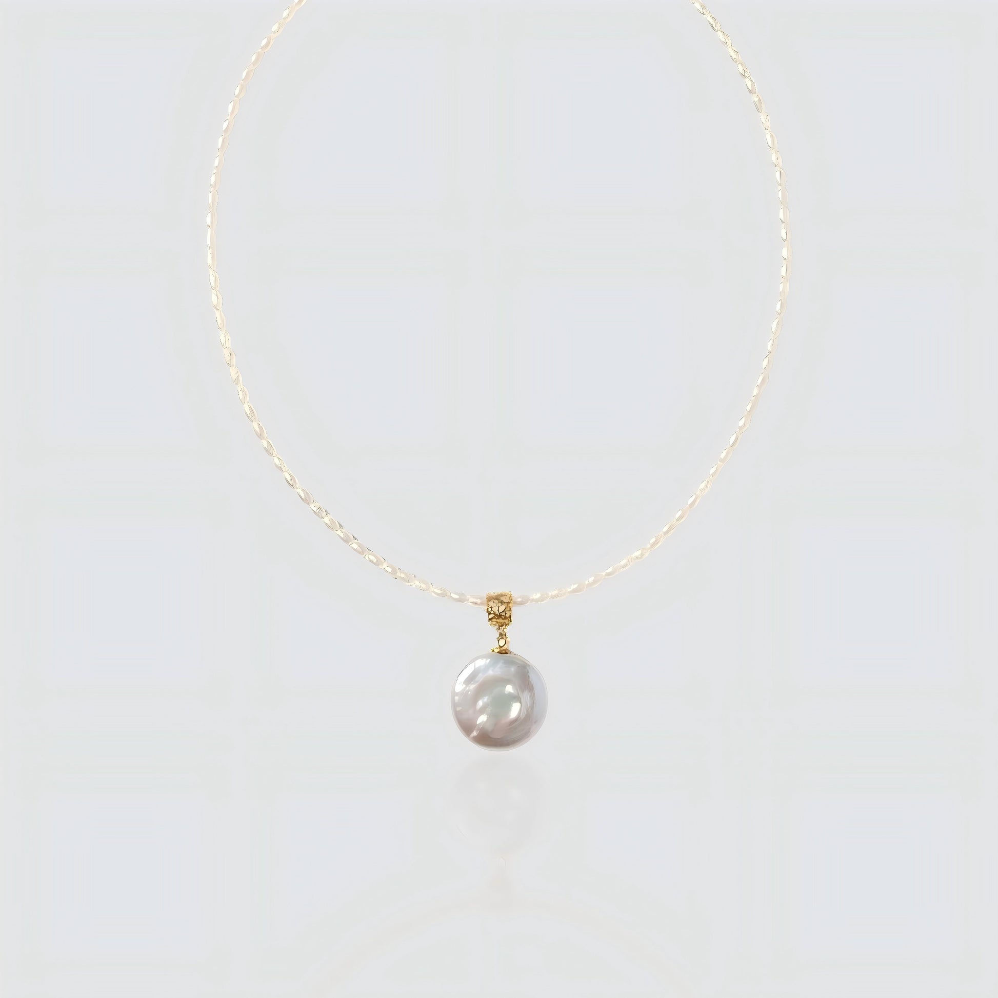 A pristine view of our delicate seed pearl strand featuring a large, lustrous coin pearl pendant with a textured gold bail.