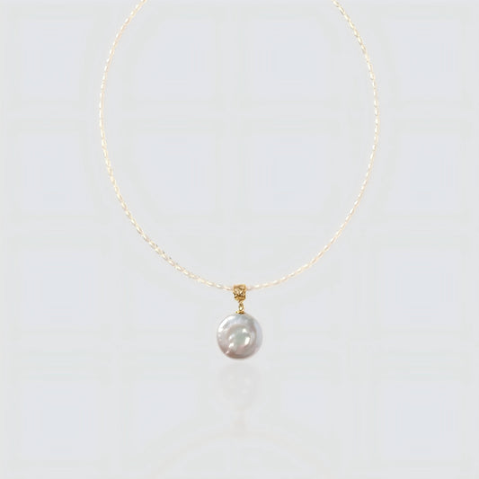 A pristine view of our delicate seed pearl strand featuring a large, lustrous coin pearl pendant with a textured gold bail.