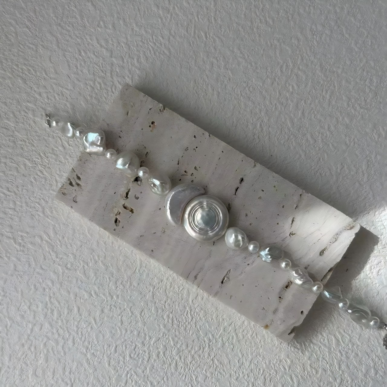 A close-up look at the iridescent inlay of the central geometric piece, contrasted with the natural, varied forms of the freshwater pearls.