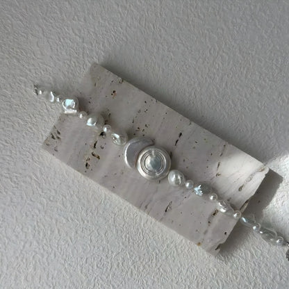 A close-up look at the iridescent inlay of the central geometric piece, contrasted with the natural, varied forms of the freshwater pearls.