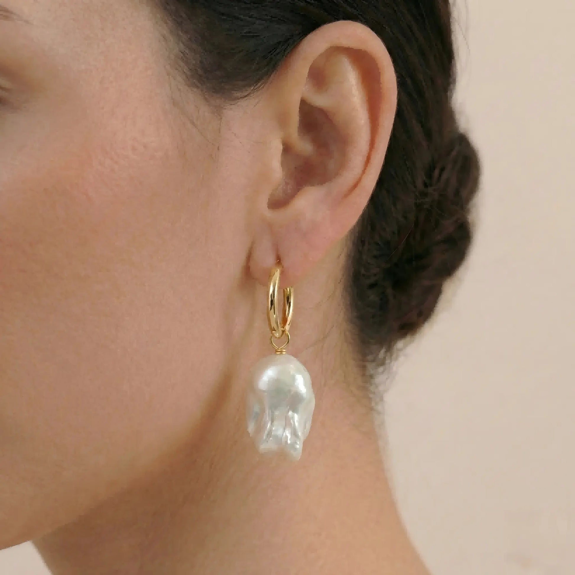 Woman wearing The Aurora Drop baroque pearl earrings showing elegant style and size on the ear with 18K gold plating shine.