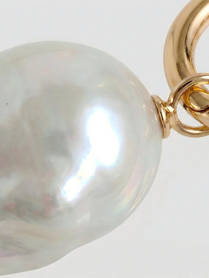 Macro close-up of a radiant natural baroque pearl attached to a polished 14k gold hoop, highlighting the gemstone's unique organic texture and high luster.