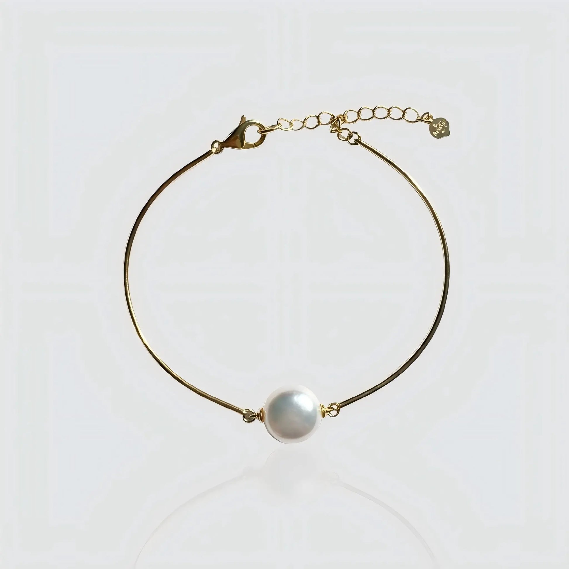 A minimalist gold wire bracelet featuring a single large white freshwater pearl in the center. The bracelet has a rigid, bangle-like shape with a lobster clasp and adjustable extension chain. Modern pearl jewelry by Pearltide.