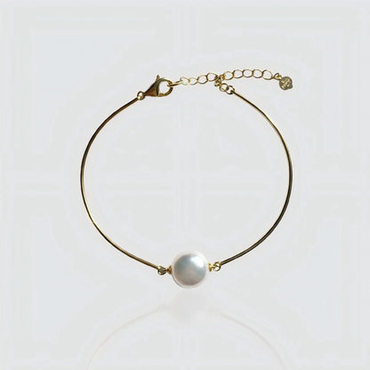 A minimalist gold wire bracelet featuring a single large white freshwater pearl in the center. The bracelet has a rigid, bangle-like shape with a lobster clasp and adjustable extension chain. Modern pearl jewelry by Pearltide.