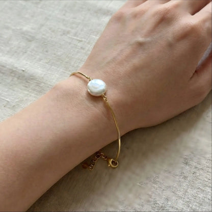 A close-up of a woman's wrist wearing the delicate gold floating pearl bracelet. The image shows how the rigid wire keeps its round shape, making the single pearl sit perfectly on the top of the wrist.