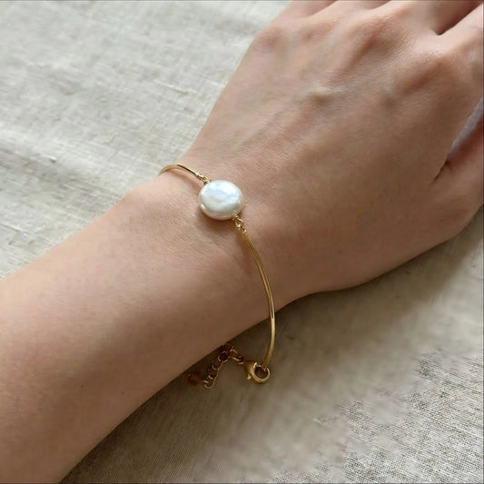 A close-up of a woman's wrist wearing the delicate gold floating pearl bracelet. The image shows how the rigid wire keeps its round shape, making the single pearl sit perfectly on the top of the wrist.