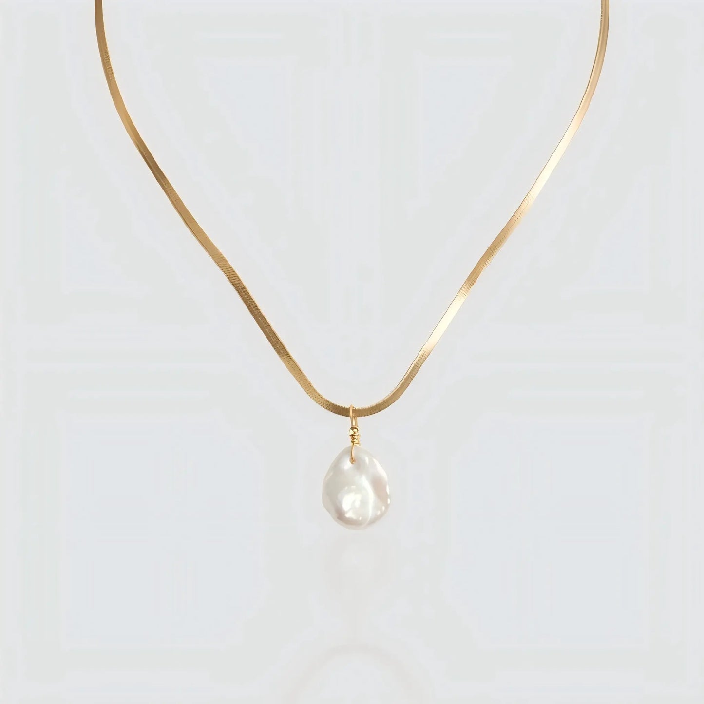 A flat gold snake chain necklace featuring a single white baroque pearl pendant isolated on a light background. The necklace has a sleek, herringbone texture that resembles liquid gold. Minimalist pearl jewelry by Pearltide.