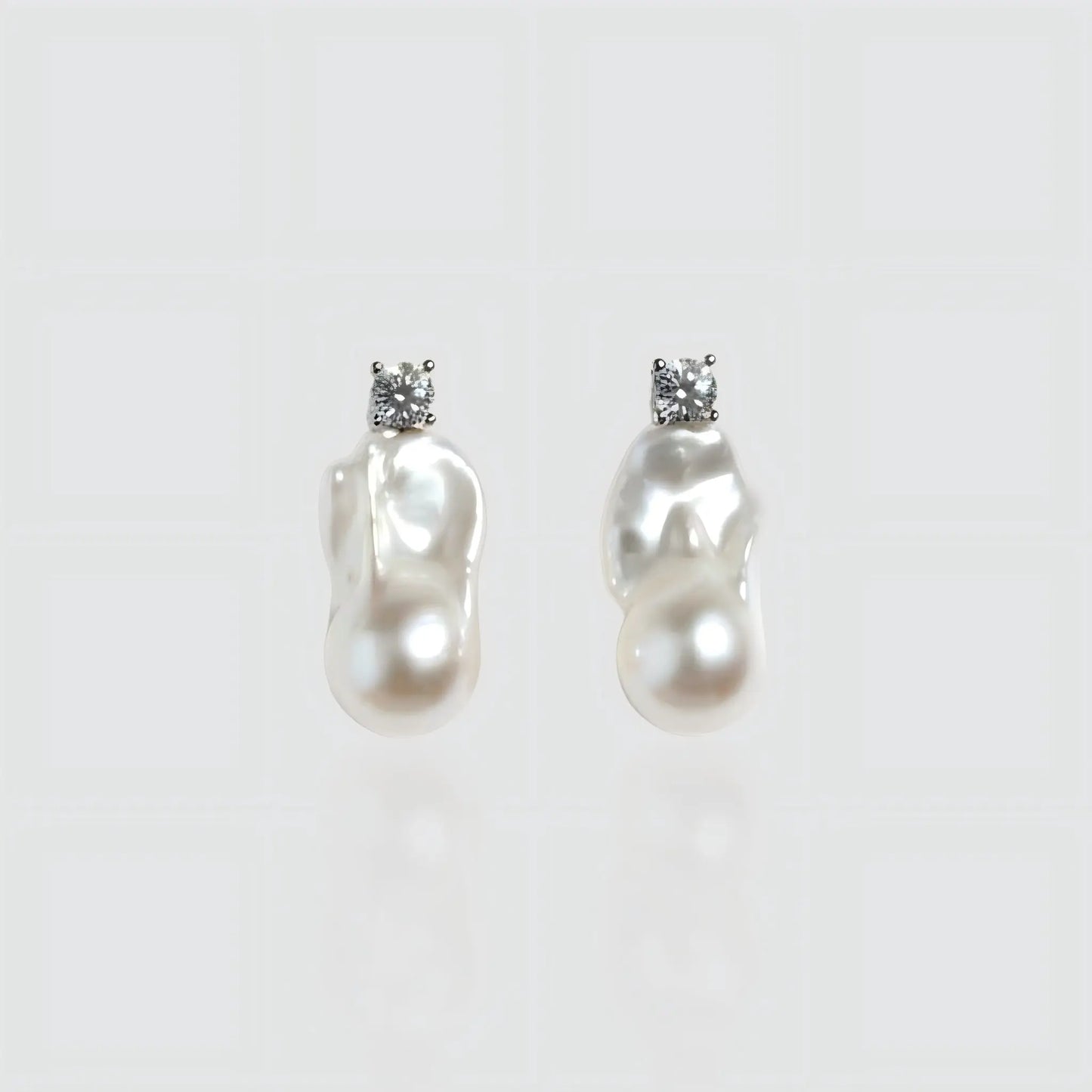 Pair of irregular shaped freshwater baroque pearl earrings with silver posts, isolated on white background.