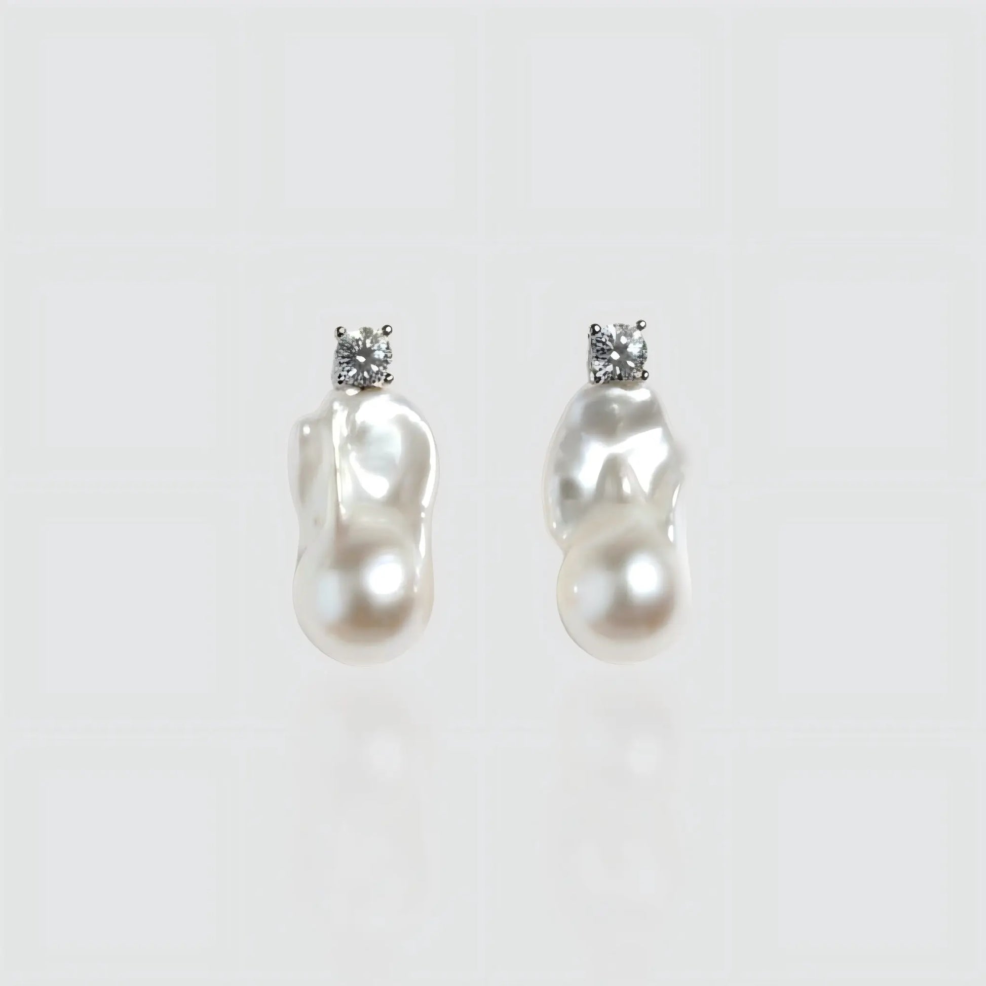 Pair of irregular shaped freshwater baroque pearl earrings with silver posts, isolated on white background.