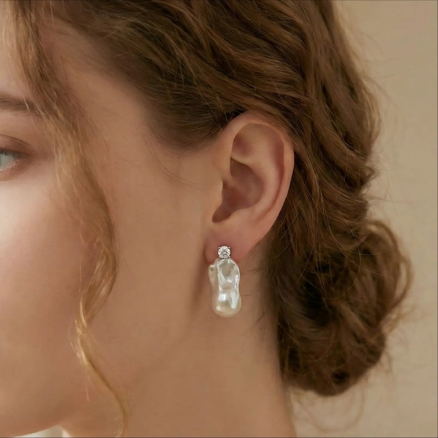 Woman wearing elegant white baroque pearl drop earrings with a diamond stud, side profile close-up.