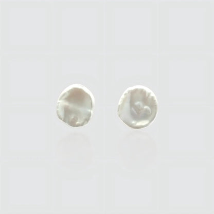 A pair of minimalist white freshwater pearl stud earrings on a light gray background. The pearls feature a flat, organic baroque shape resembling petals or coins with a high, creamy luster. Simple and elegant jewelry by Pearltide.
