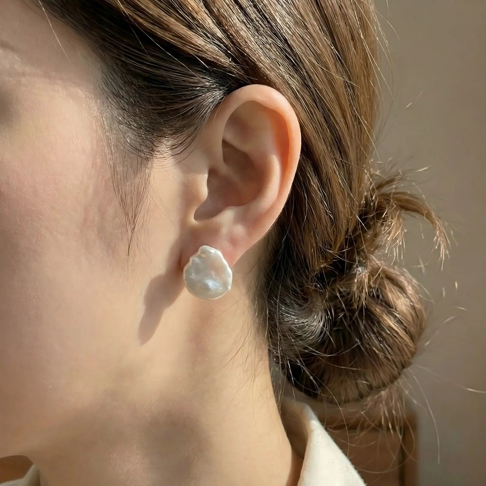 A close-up side profile of a woman wearing the Pearltide organic pearl stud earrings. The image shows how the flat baroque pearl sits comfortably flush against the earlobe, offering a modern and subtle glow suitable for everyday wear.