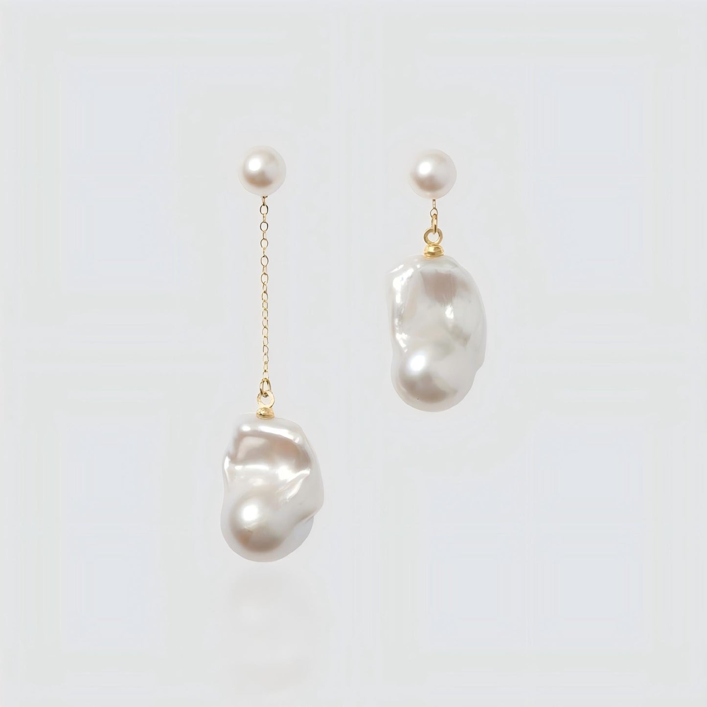 Pair of asymmetrical freshwater pearl earrings on a white background. Left earring features a long gold chain drop, while the right earring is a short drop, both with round pearl studs.