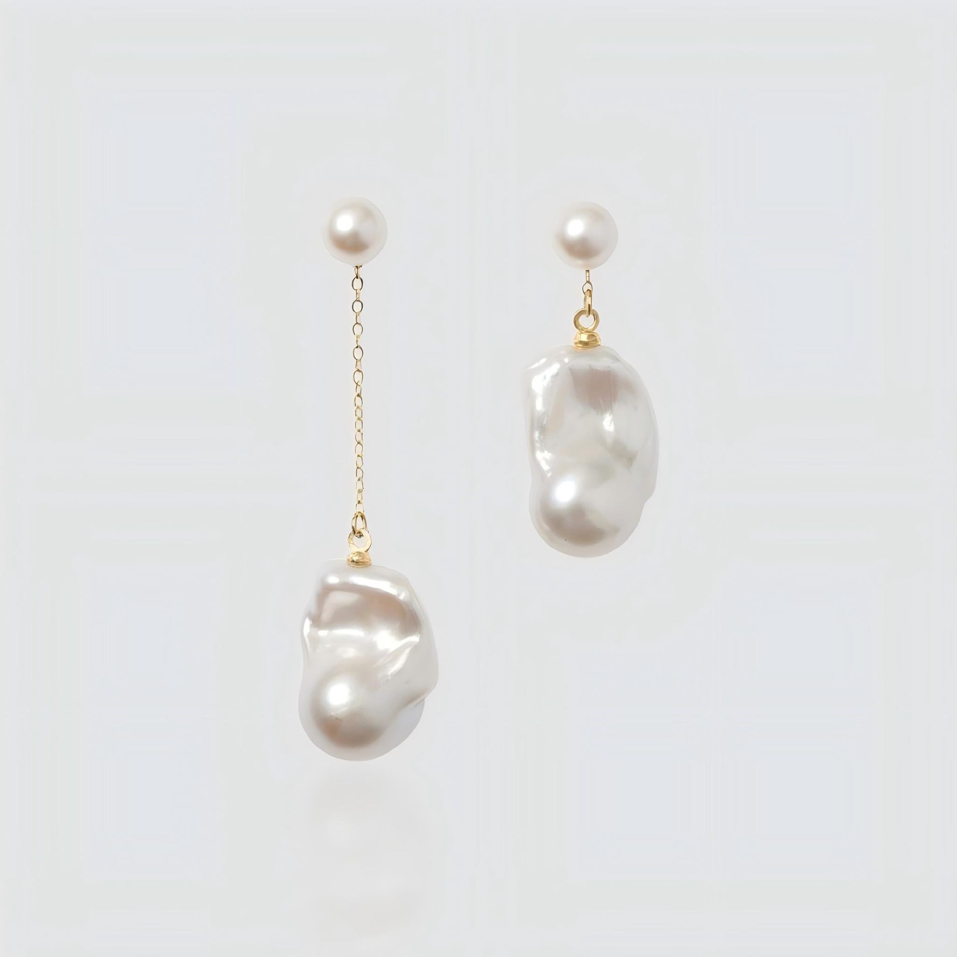 Pair of asymmetrical freshwater pearl earrings on a white background. Left earring features a long gold chain drop, while the right earring is a short drop, both with round pearl studs.