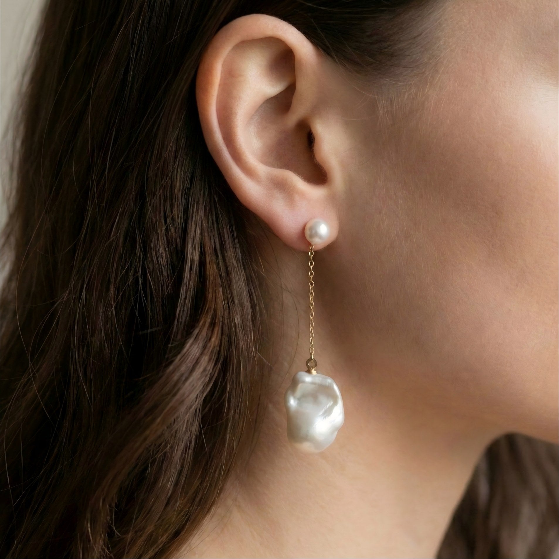 Model wearing mismatched baroque pearl earrings to show the length difference. One side hangs low on a chain, the other sits closer to the earlobe.